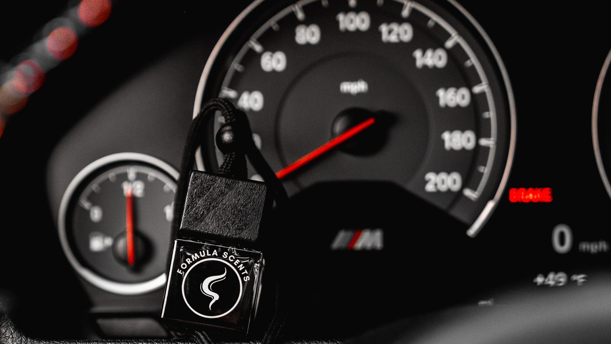 Un flacon Formula Scents suspendu devant le compte-tours d'une BMW M, l'aiguille rouge sur le cadran