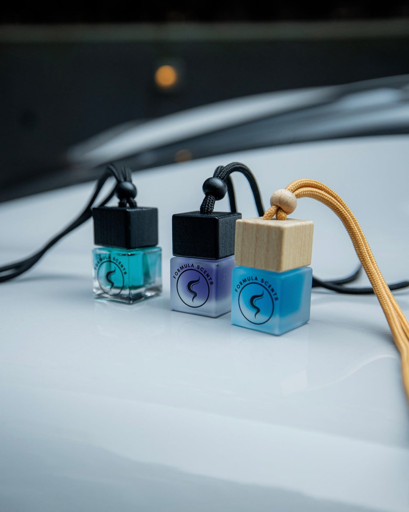 Trois flacons Formula Scents, verre transparent, fumé et bouchon de bois clair, posés sur un capot blanc